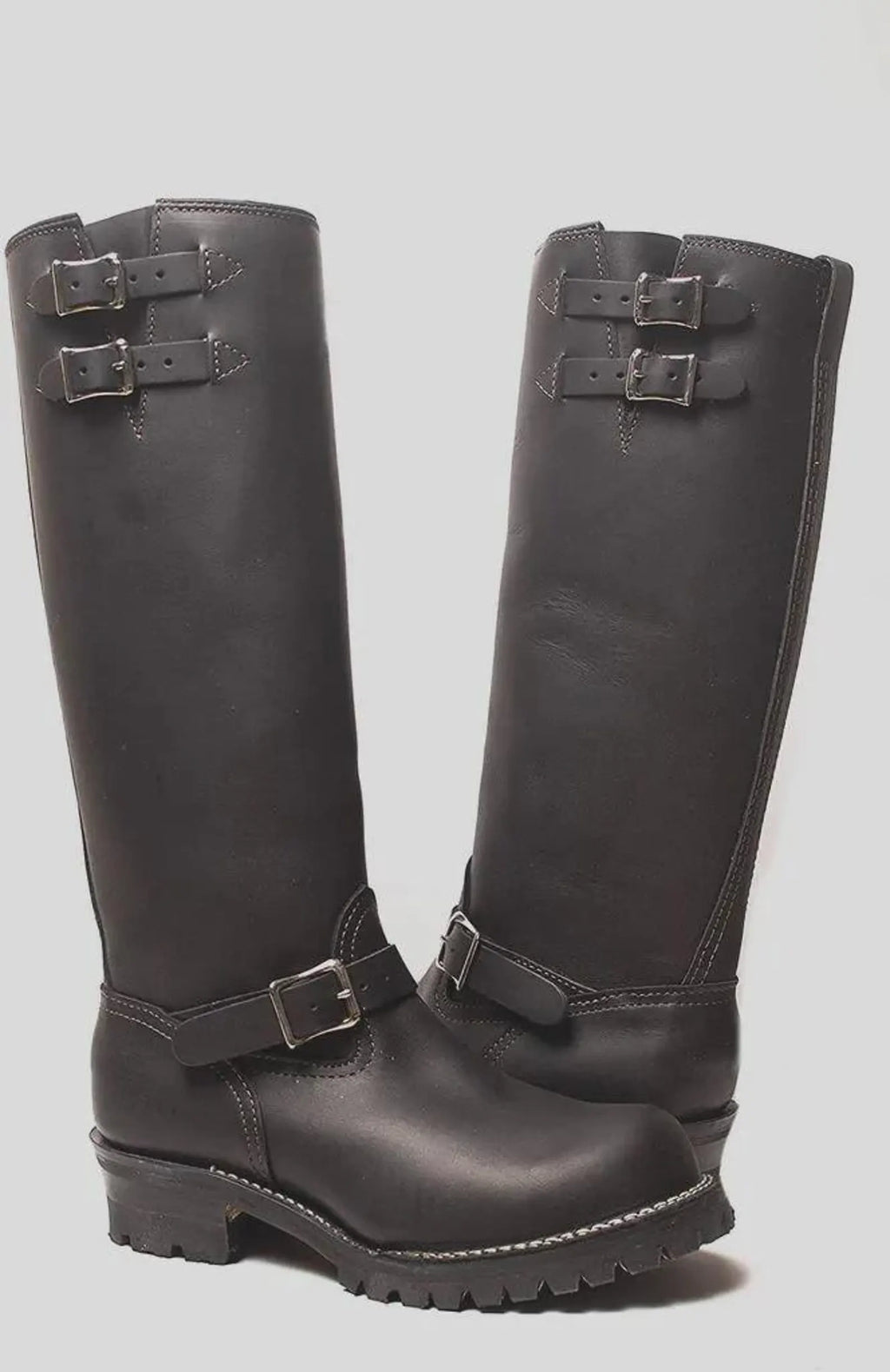 Pair of black knee-high Double Strap Leather Biker Boots with buckles on a light gray background